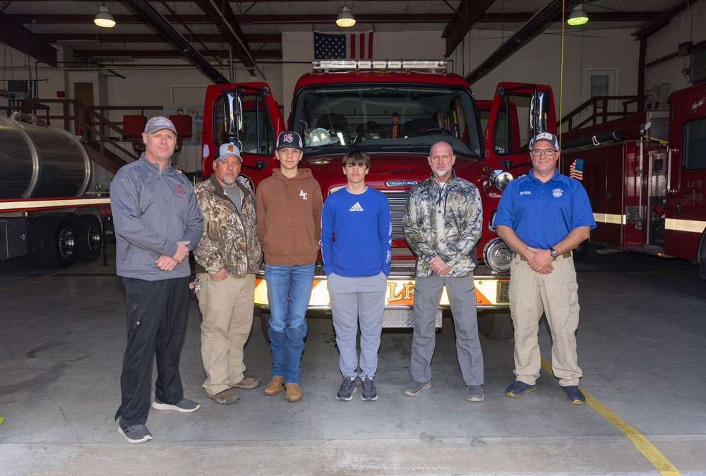 Four men and two boys standing in front of the front of a fire truck.