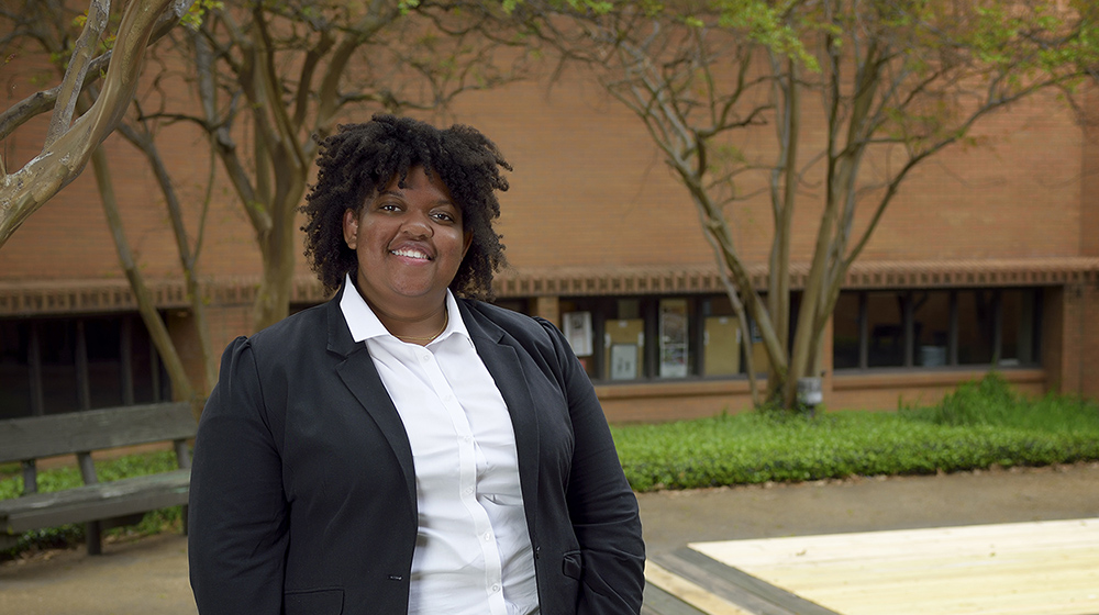 A young woman wearing a white collared shirt and dark blazer smiles at the camera.