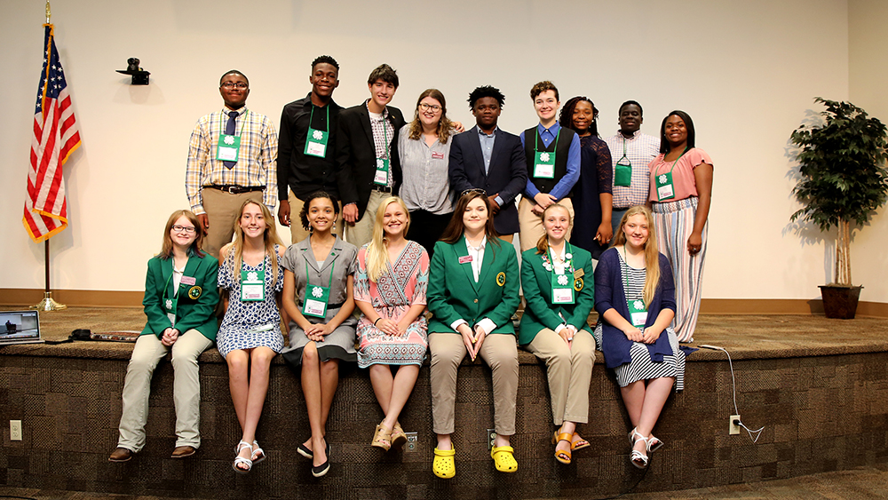 A group of sixteen students post for a picture on a stage. 