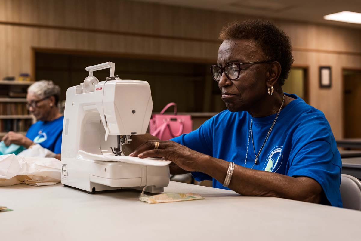 A woman with dark hair wearing a blue shirt working at a sewing machine.