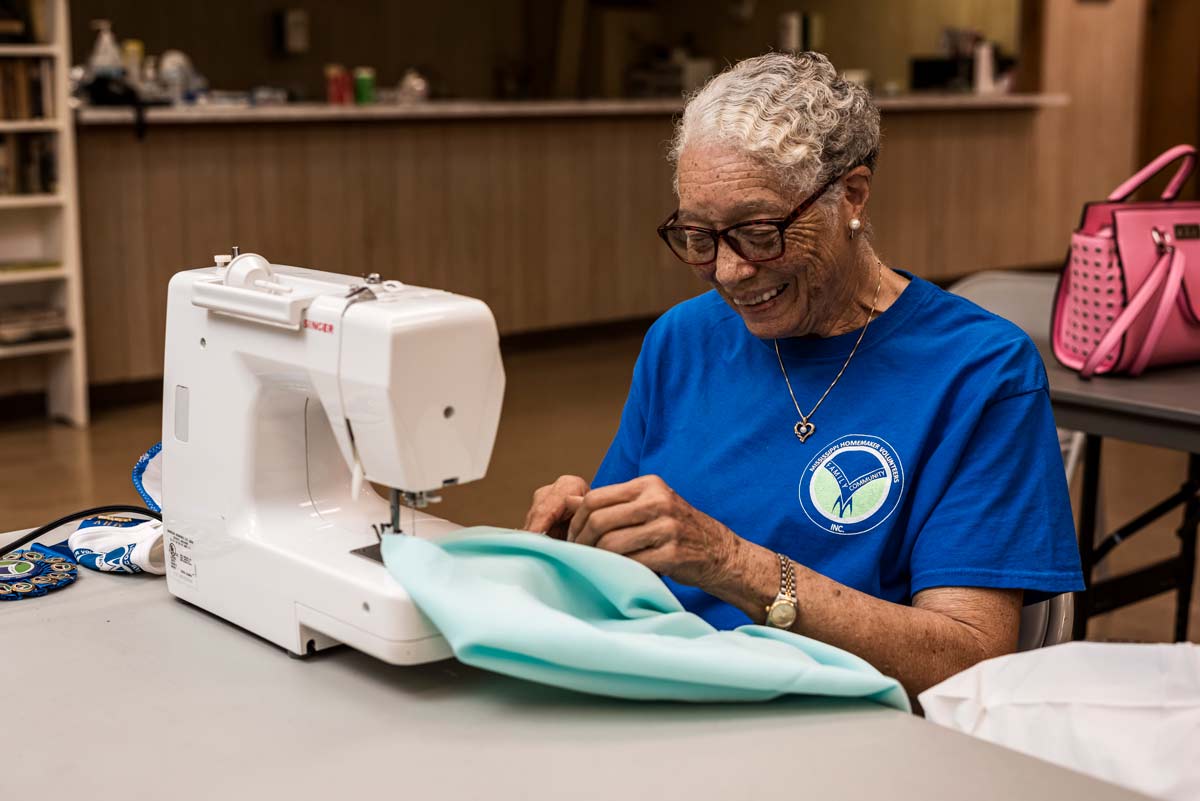 A woman with white hair wearing a blue shirt working at a sewing machine.