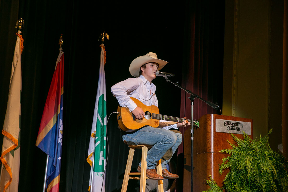 A teenage boy singing into a microphone and playing guitar.