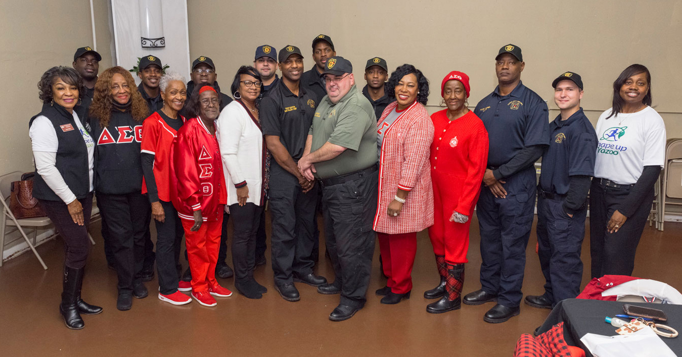 A large group of people, including women that are wearing sorority swag and men that are wearing fire department uniforms.