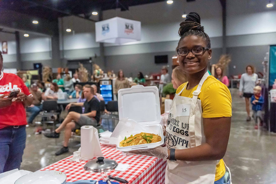 A girl smiles, holding a white tray of food.