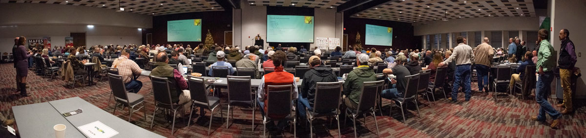 A panoramic image of a large crowd of people with two large screens in the back.