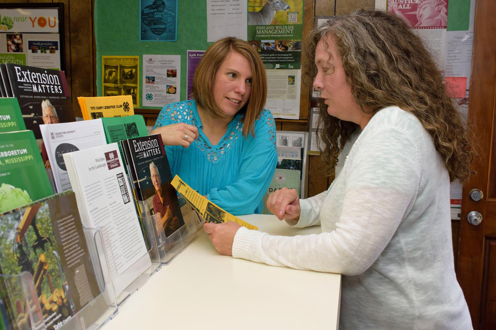 Woman in blue shirt talks to woman holding a brochure