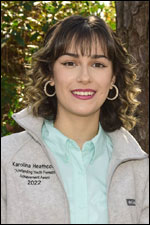 A brunette girl wearing a gray jacket and blue polo, smiling.