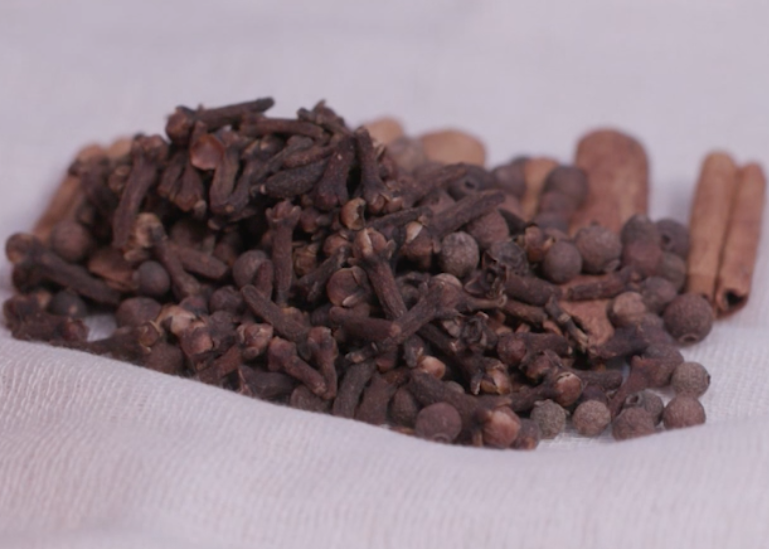 Whole spices, including cloves, allspice and cinnamon sticks, on a piece of white cheesecloth. 