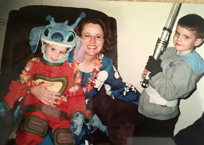 Children in Disney Halloween costumes pose for a photo with a female relative who is also wearing a costume.