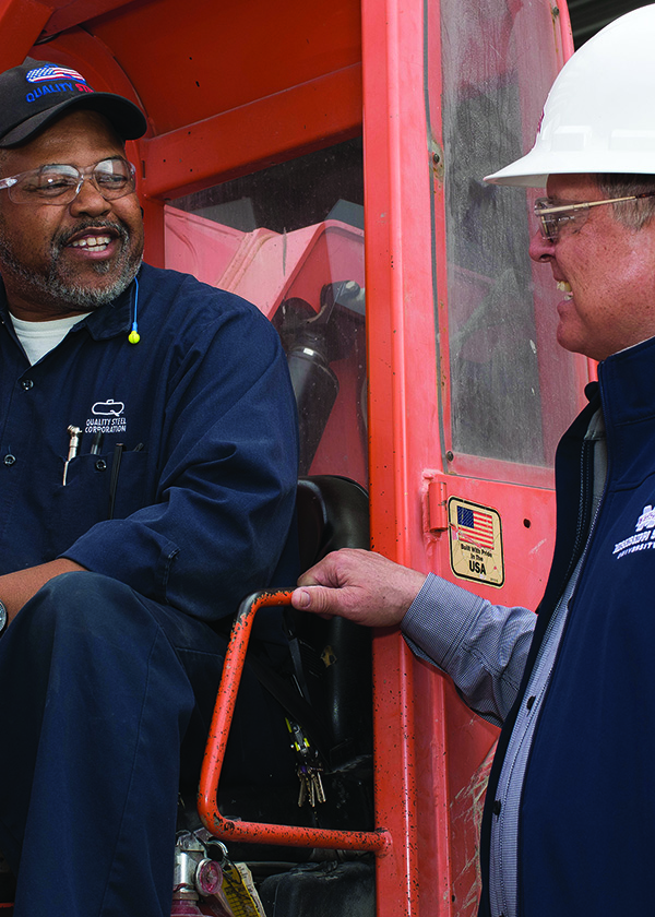 Two smiling men on a large red piece of equipment.