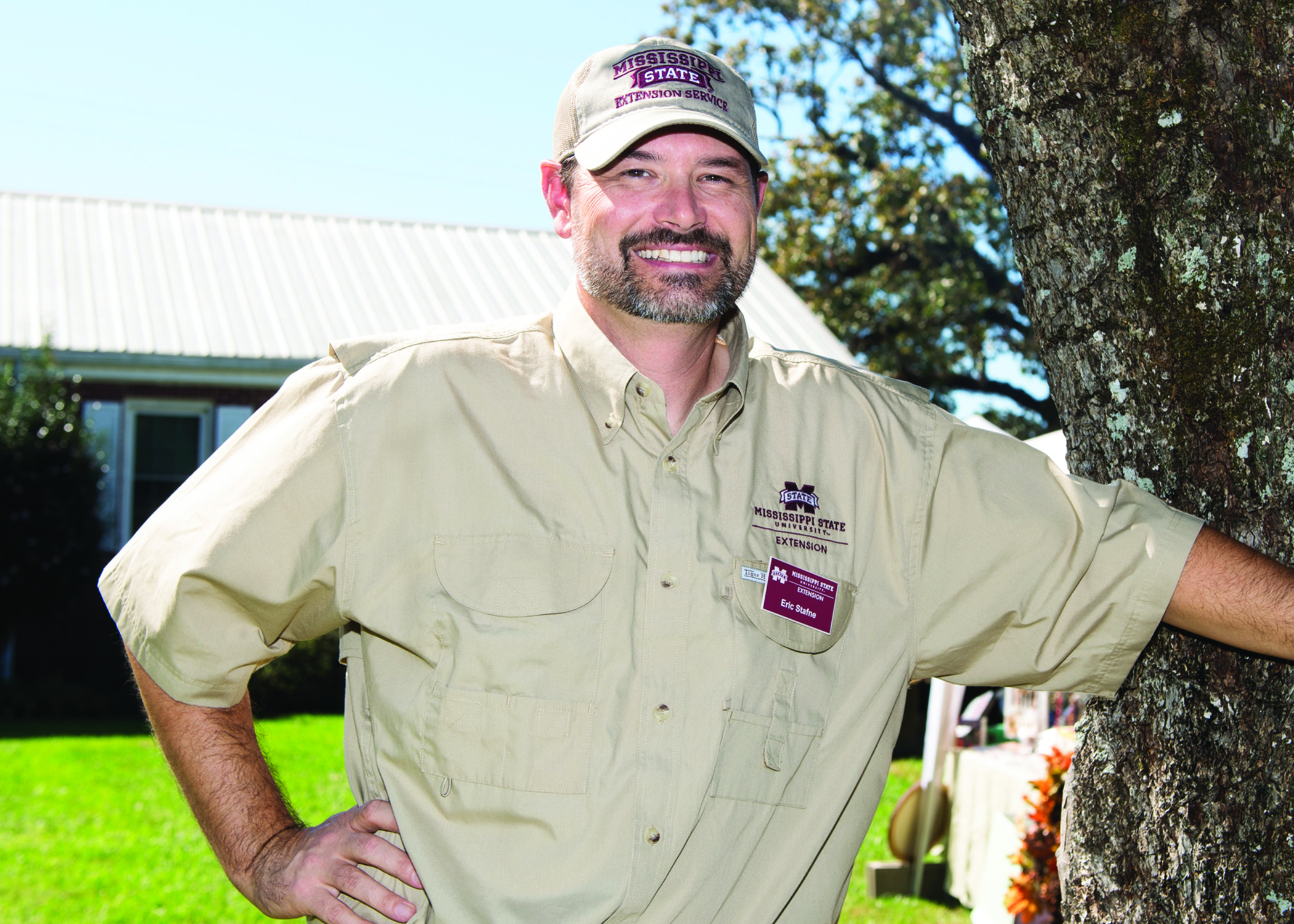 Exension specialist smiles while leaning on a tree.