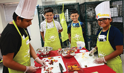 Four youths in aprons cut up fruit and smile at the camera.