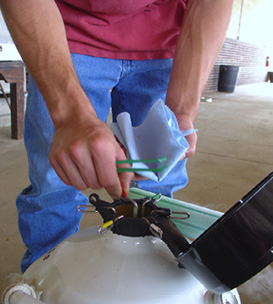 A person lifts a canister from a tank with one hand and holds a paper towel in the other.