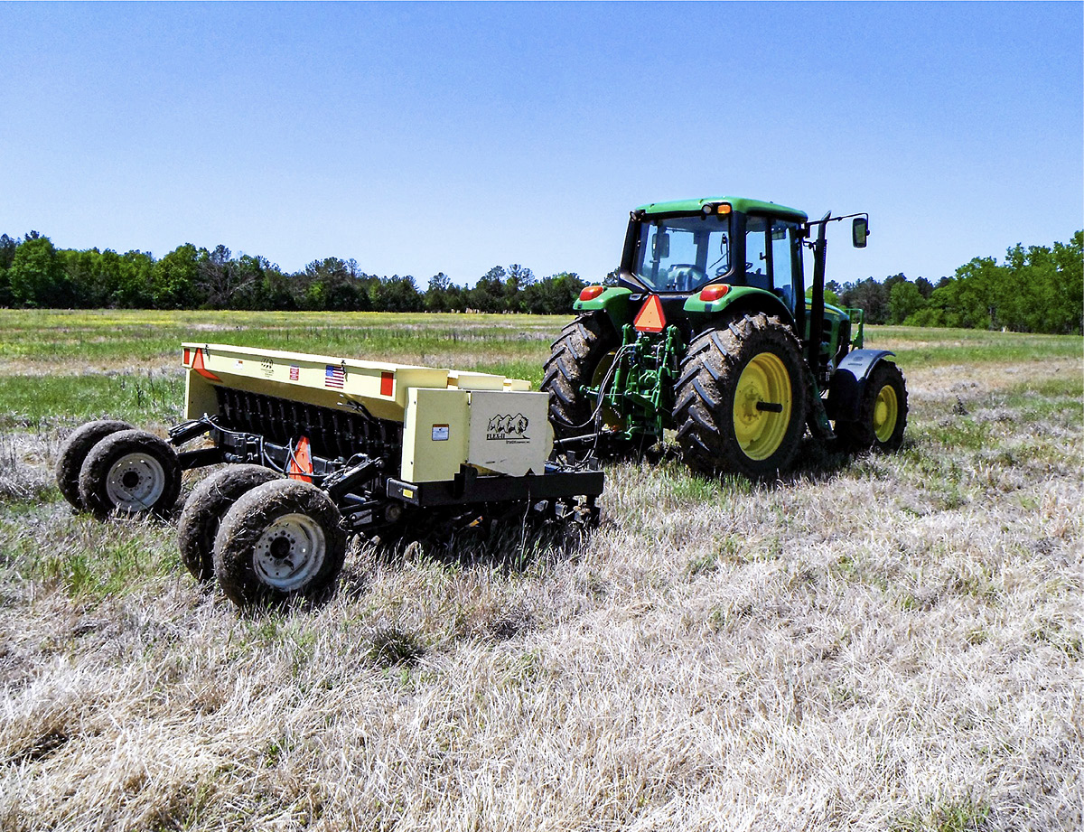 A tractor pulls a grass seed drill across a field.