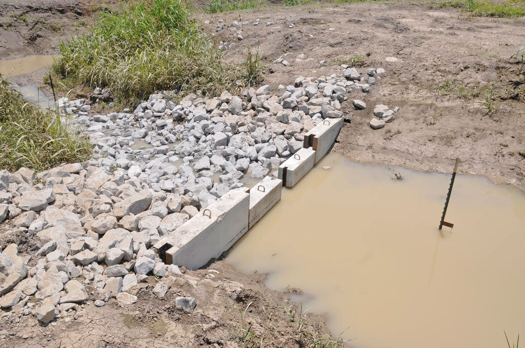 A short wall made of concrete slabs with large rocks on one side and muddy water on the other.