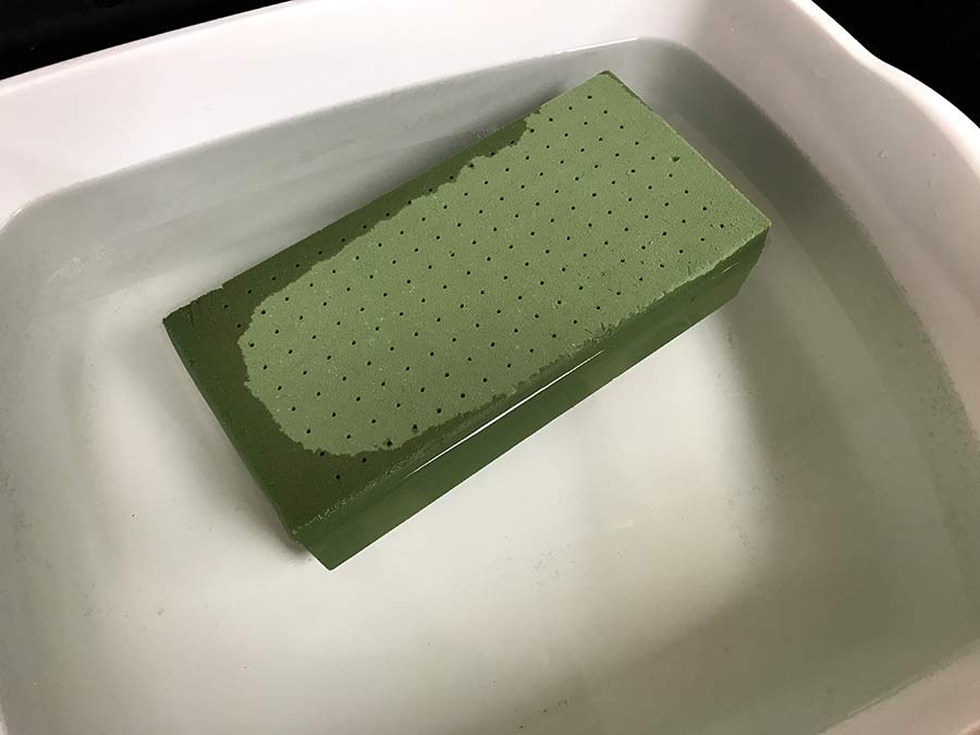 A brick of floral foam half submerged in water.