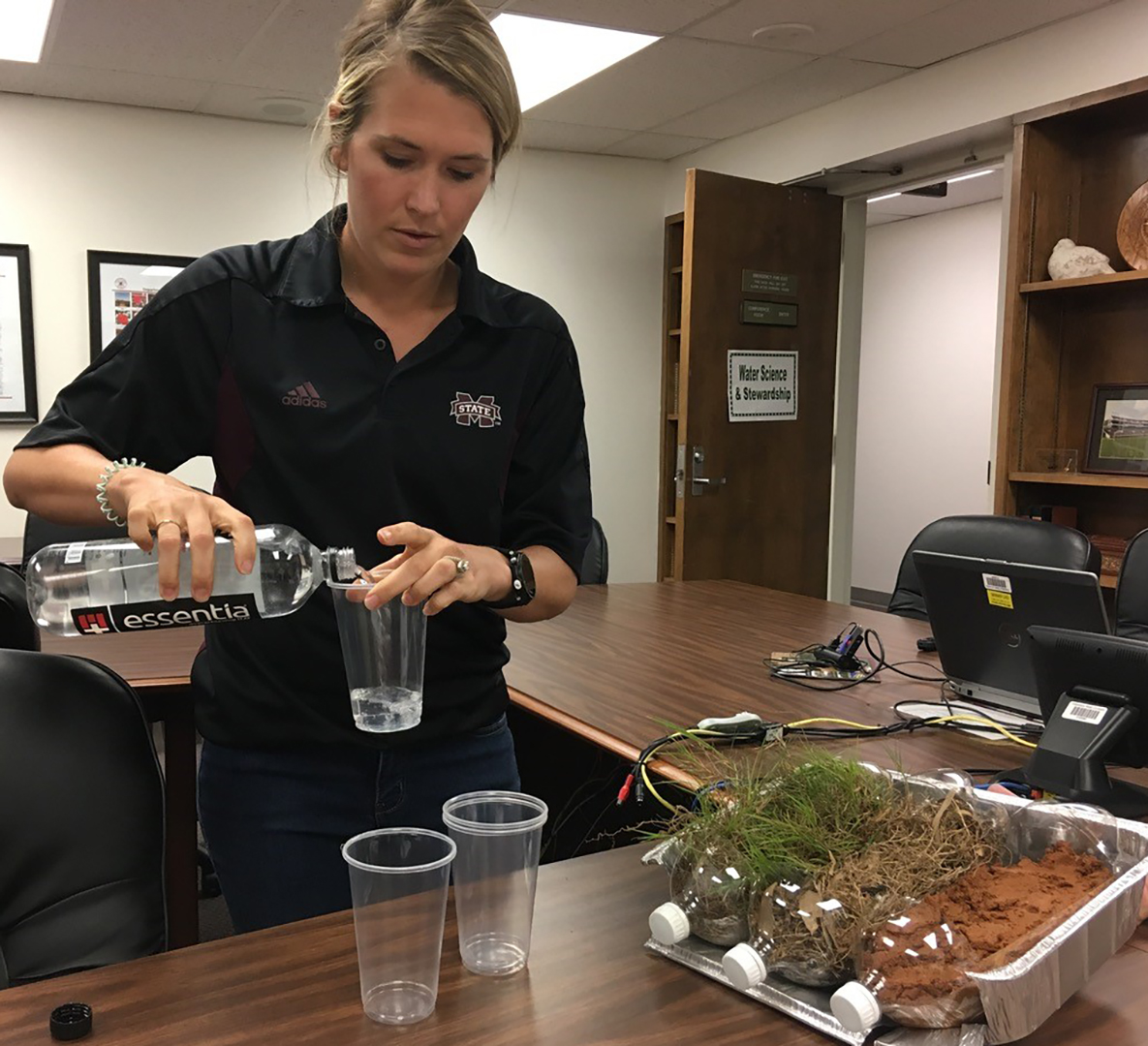 A woman pours water into three plastic cups.