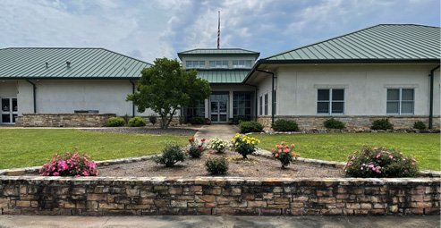 A building with a flower bed in front with several rose bushes spaced apart. 