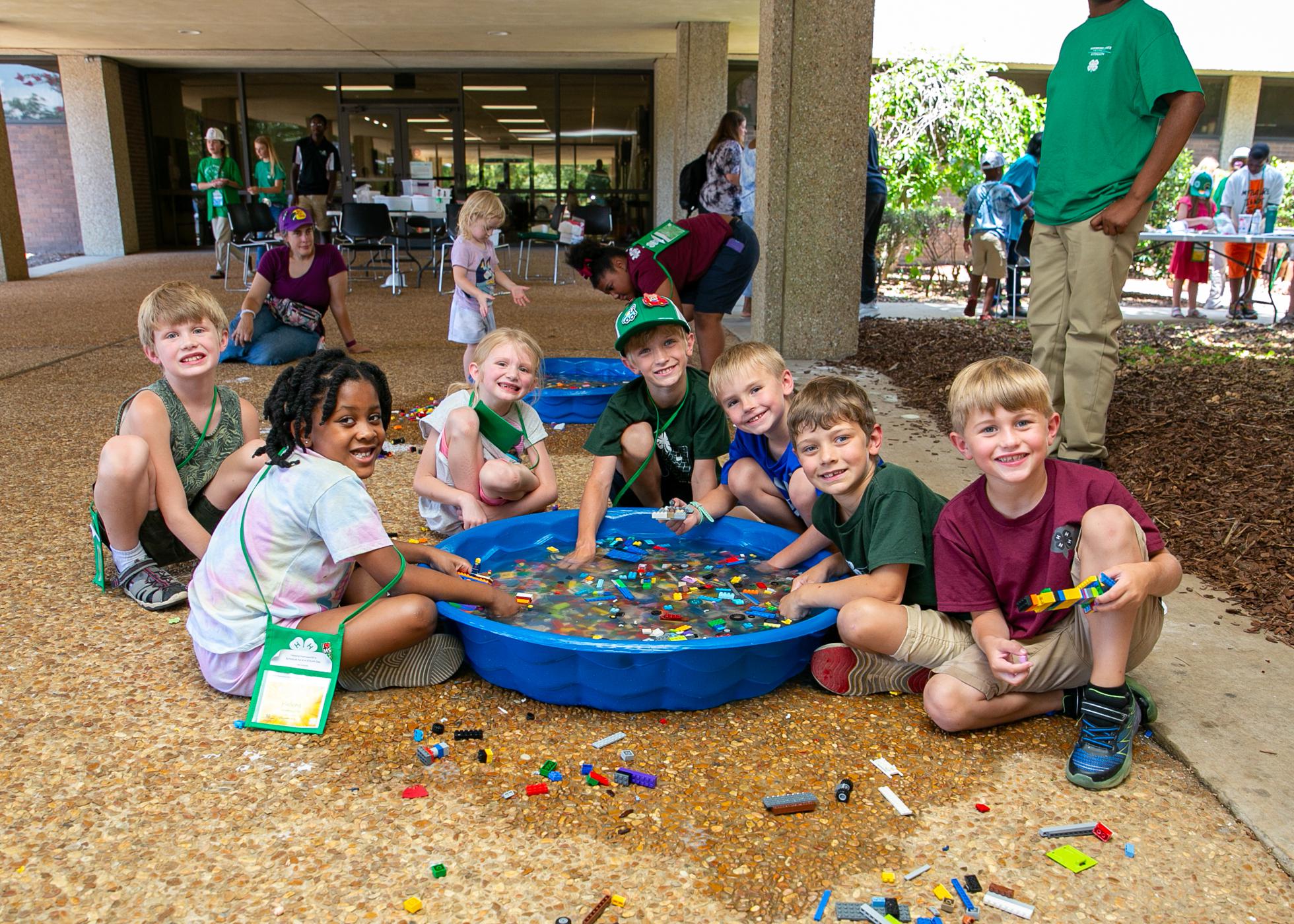 Seven young children playing with legos in a small pool of water.