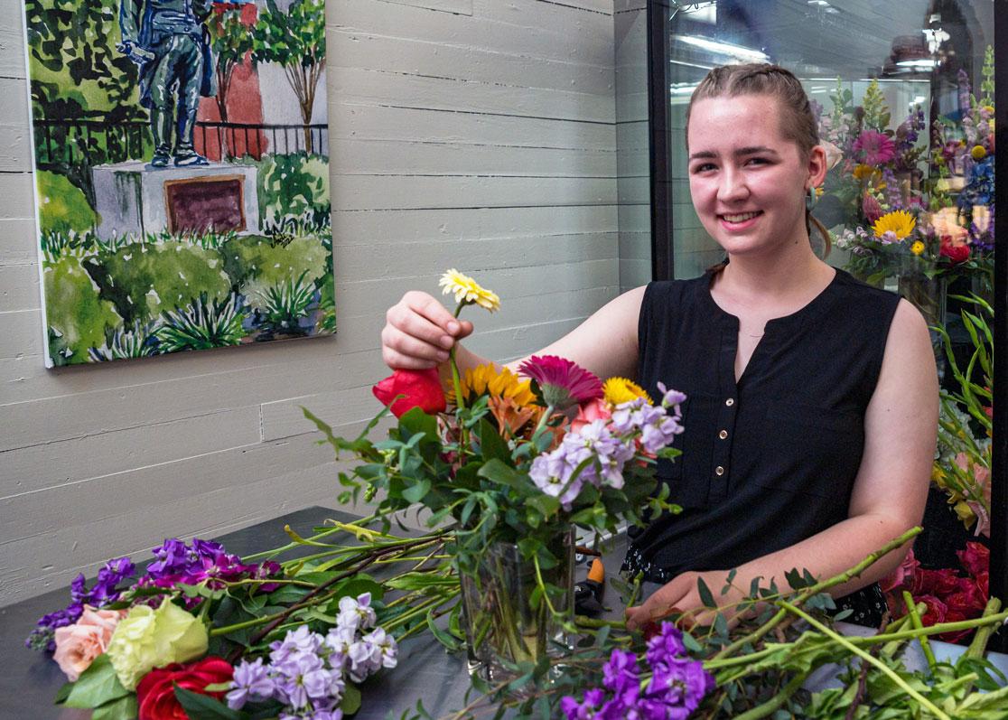 A young woman smiling while arranging a bouquet of flowers.