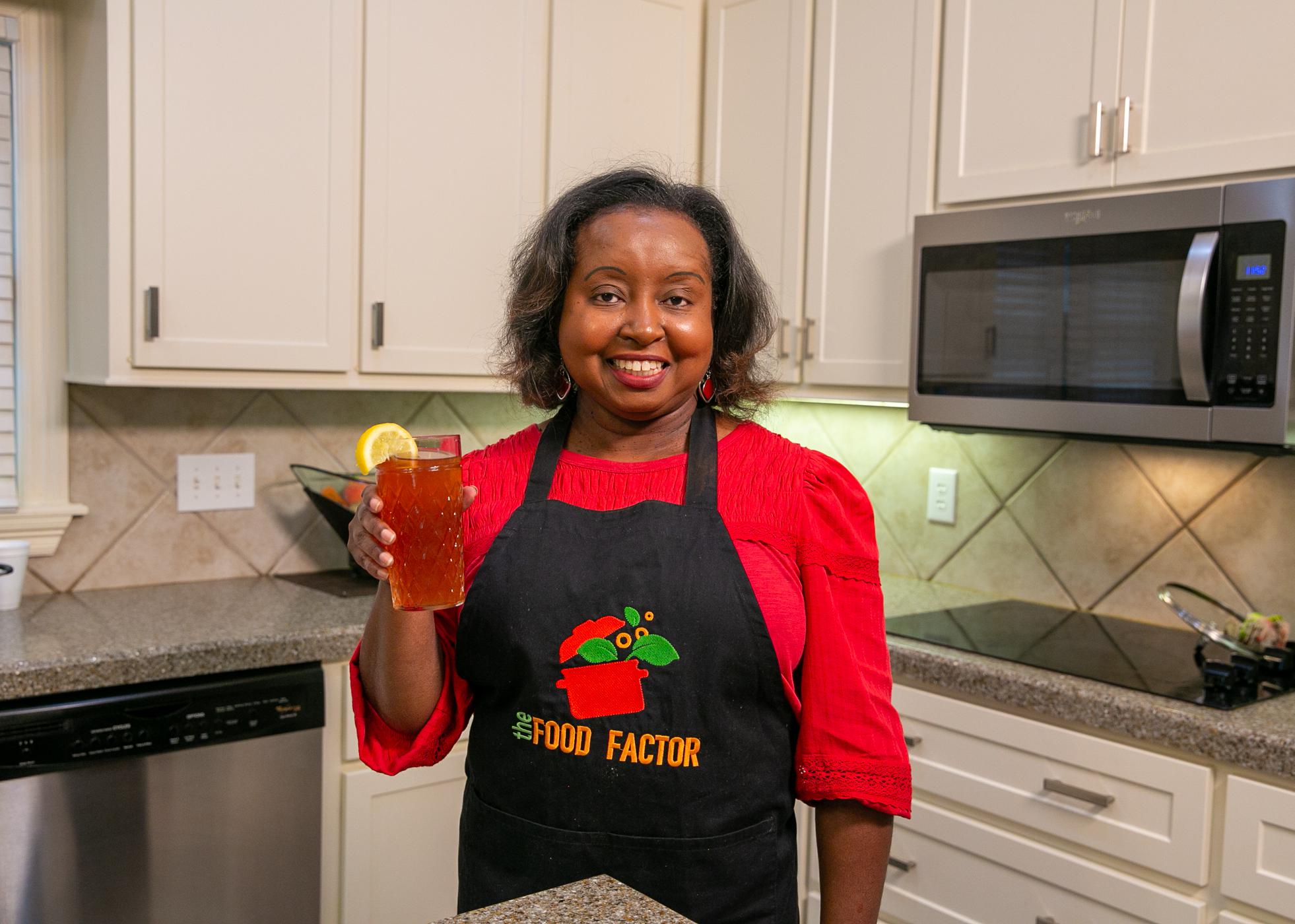 A woman holds a glass of strawberry gree tea in a kitchen.
