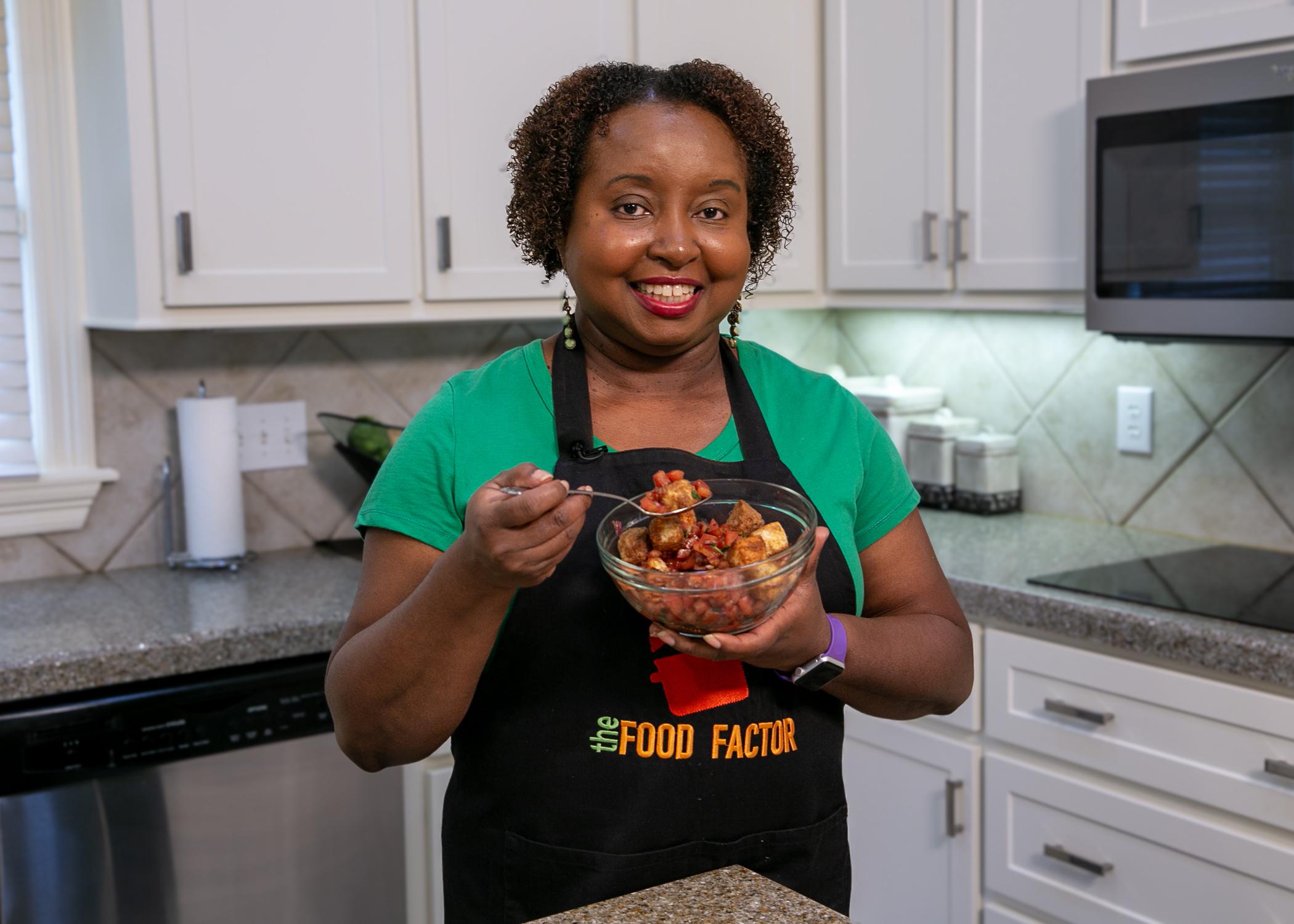 A woman in a kitchen holds a bowl of bruschetta salad.