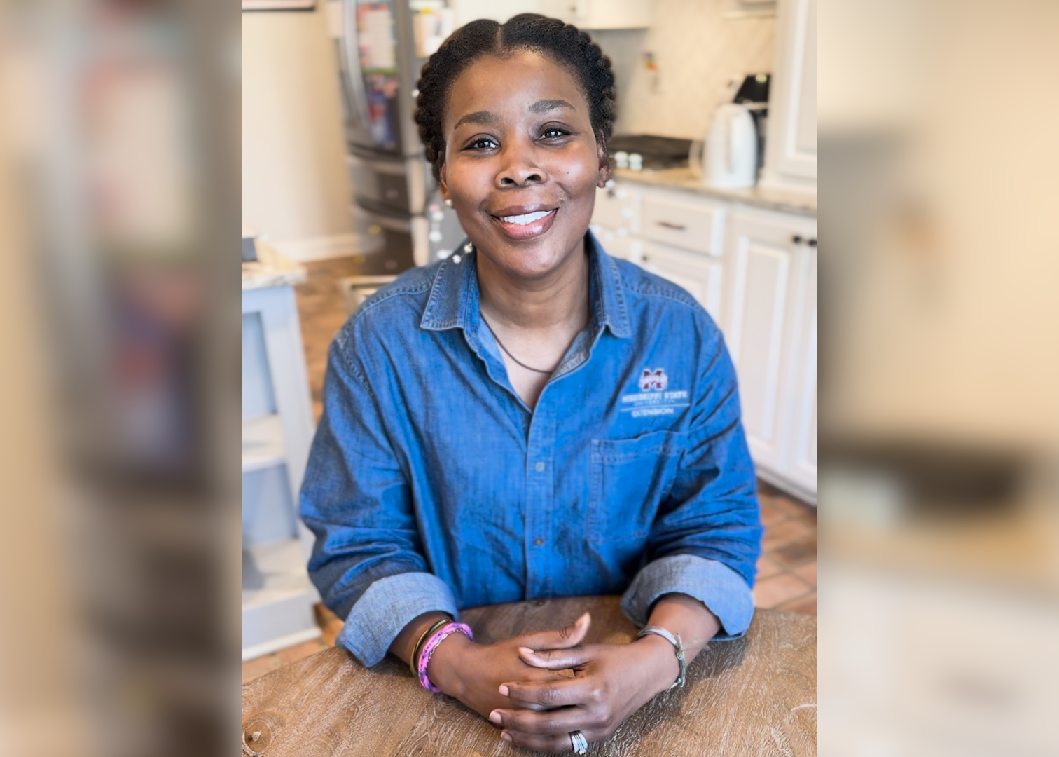 A woman sits at a kitchen table and smiles for the camera.