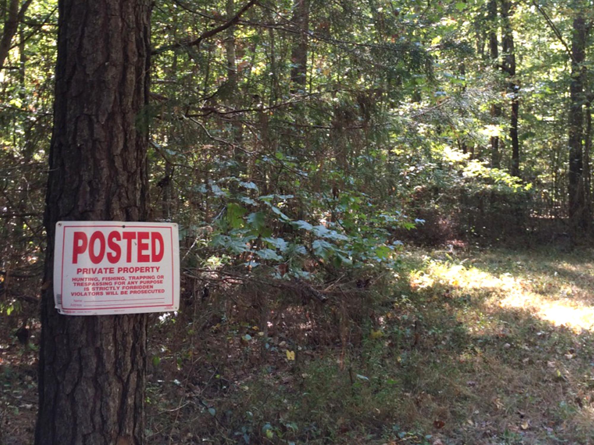 A sign nailed to a pine tree in a wooded area that reads, “POSTED PRIVATE PROPERTY.”