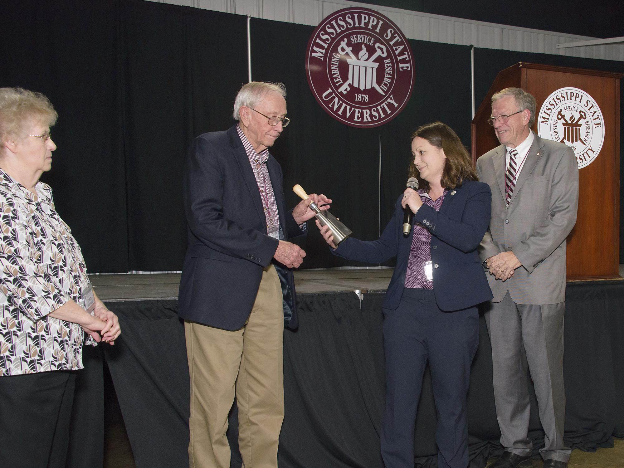 Woman handing man silver cowbell and shaking his hand.