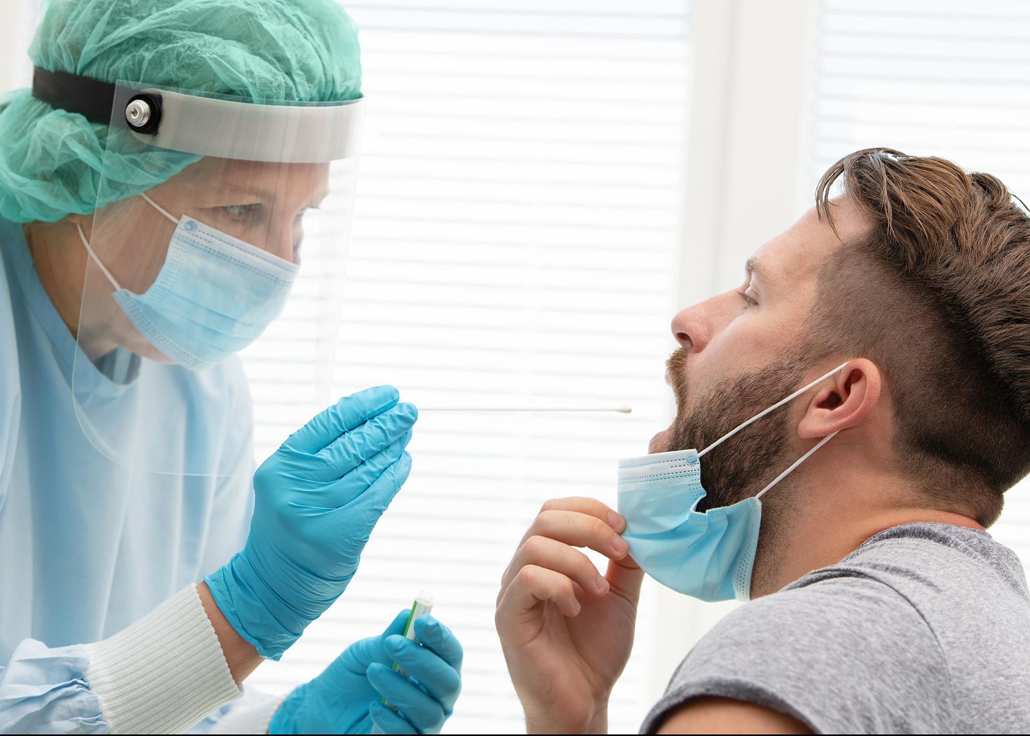 Medical worker in protective clothing takes a throat swab from a male patient.