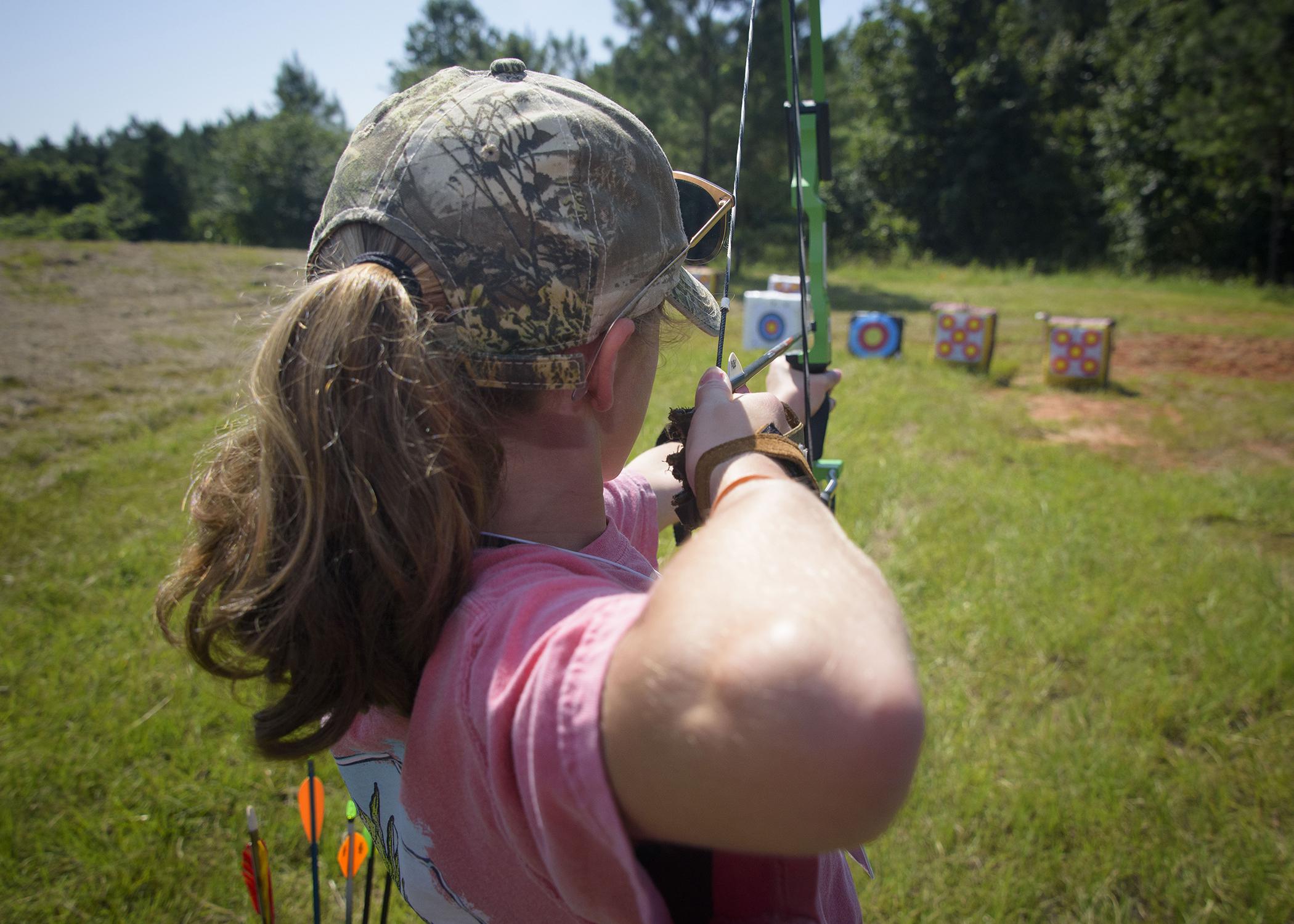 A young person pulls back a bow while aiming at a target.