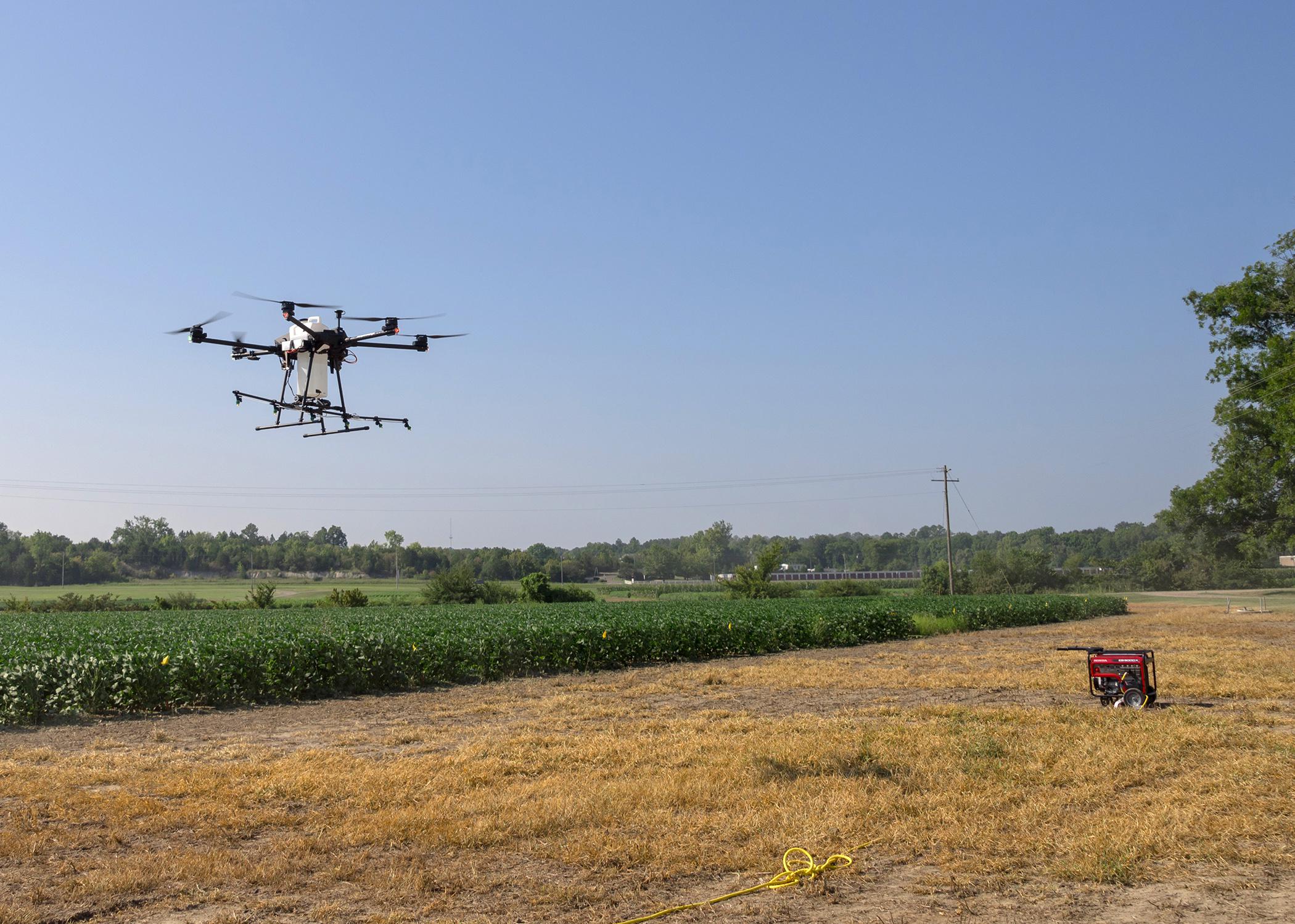 A large drone hovers over cropland.