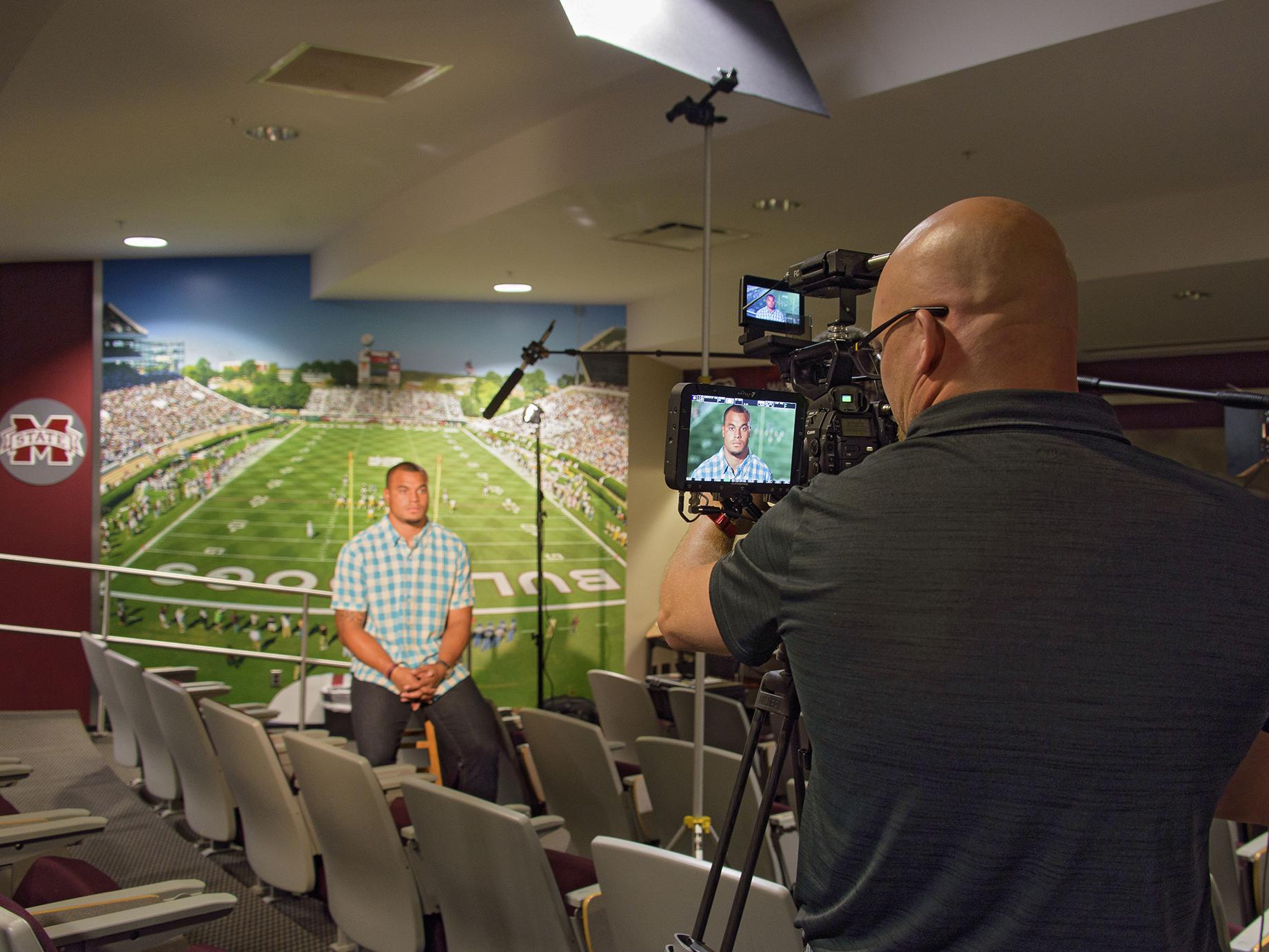 Brian Utley, video producer with MSU Extension’s Agricultural Communications, focuses a camera on former MSU football quarterback Dak Prescott in July 2016. Prescott is the face of the 2017 Public Service Announcement campaign for the 70x2020 Colorectal Cancer Screening Initiative. (Photo by MSU Extension/Kevin Hudson)