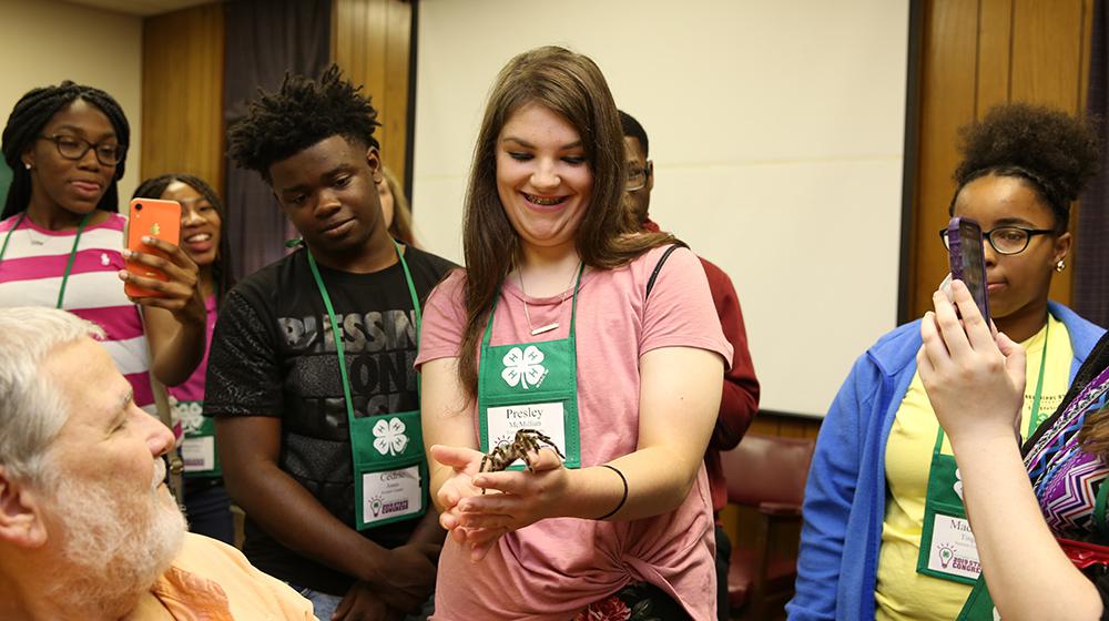 Girl holding spider while group of young people looks on.