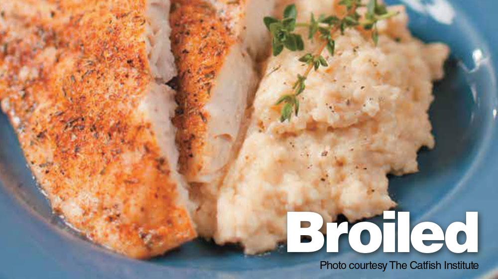 Close-up of seasoned, cooked catfish served on a plate with a potato side dish.