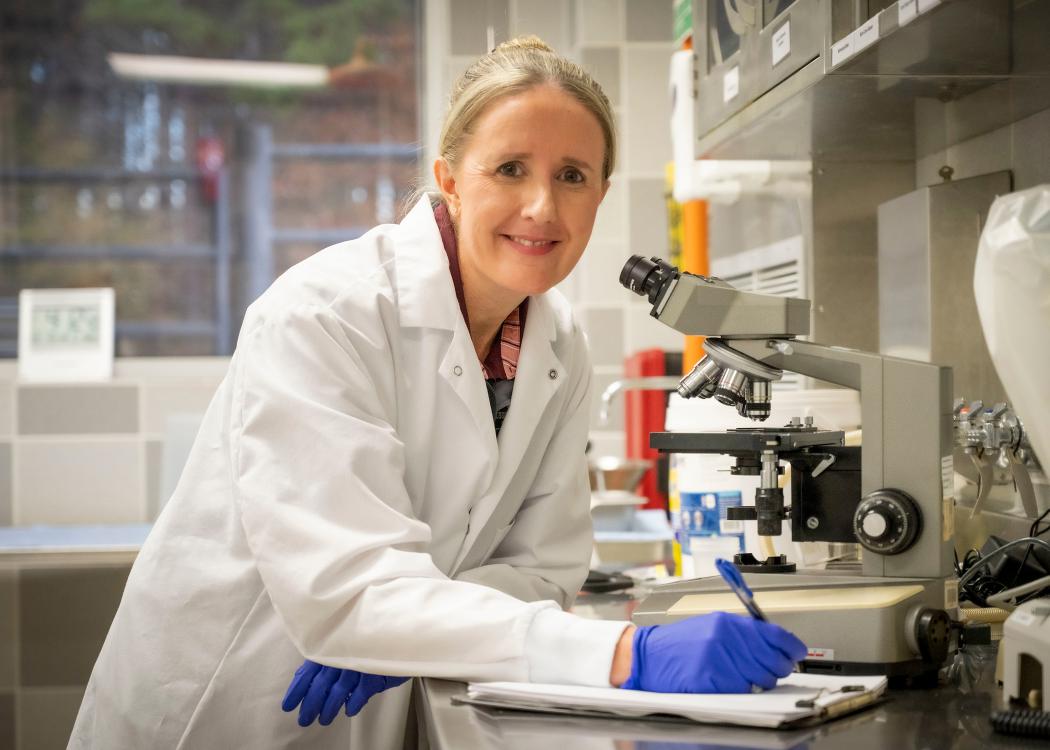 Doctor in a white coat smiling and standing beside a microscope