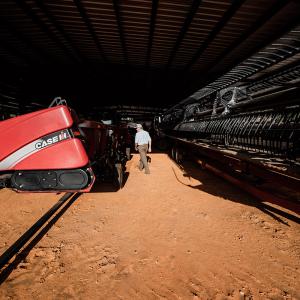 A man walking through a barn with agricultural equipment on either side.