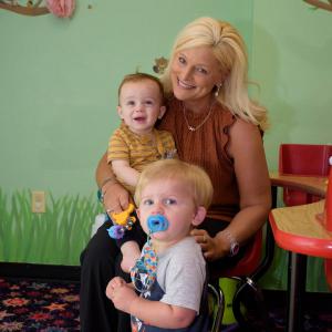 A sitting woman holding a baby with a toddler standing in front.