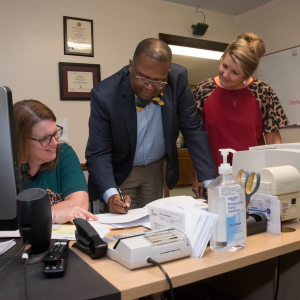 Two women look on as a man adds his signature to a document.