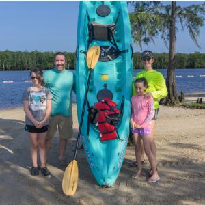 A man and woman with two girls standing in front of a kayak.