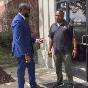 Two men talking, one with his hand extended.