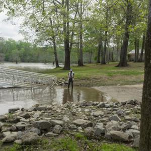 A man stands in a few inches of water at a boat ramp.
