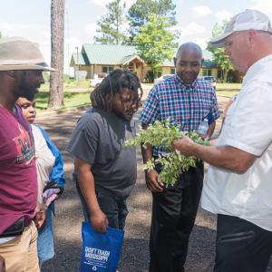 A group of people examines a plant with flowers being held by a person.