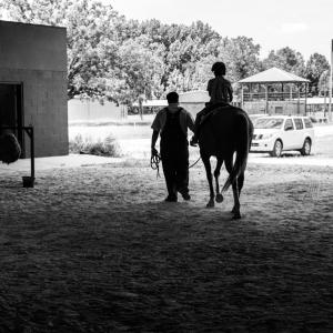 A boy riding a horse, accompanied by a man, riding away from the camera.