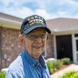 A man wearing a Korea Veteran baseball hat smiles.