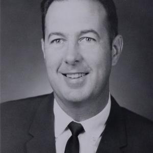A black and white headshot of a man wearing a suit and smiling.
