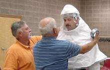 Kipp Brown, left, Extension area livestock agent based in Carroll County, assists Al Fulton, safety officer with the Mississippi Board of Animal Health, as they adjust the security hood on Charlie Stokes, area agronomics crops agent based in Monroe County. (Photo by Linda Breazeale)