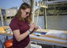 A woman standing on a boat writes on a glass vial.