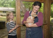 A woman holds a brown and white chicken while a young girl looks on.