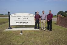 Three men stand beside a white sign on a cloudless day. The sign reads “Delta Research & Extension Center, West Farm, Mississippi Agricultural and Forestry Experiment Station, Mississippi State University.”